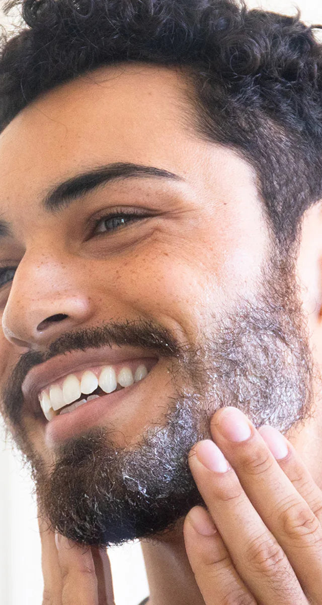 A man applying beard care product to his beard, smiling.