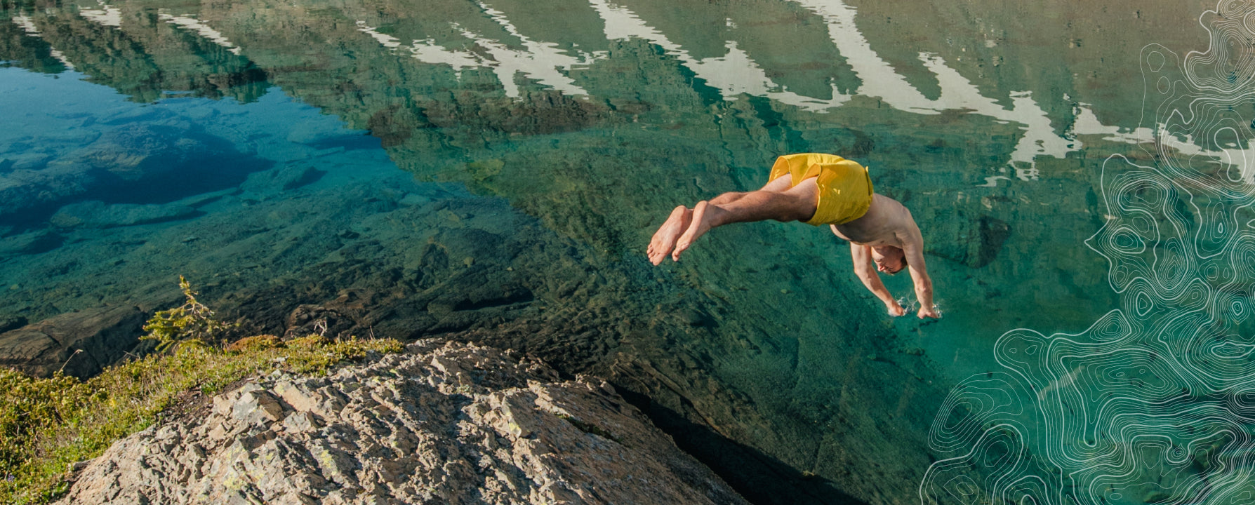 A man diving into clear, blue water from a rocky edge.