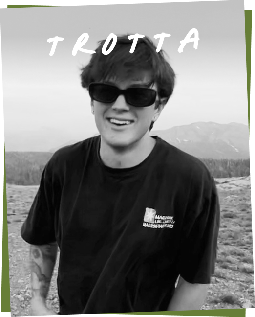 A person named Trotta wearing sunglasses and a black t-shirt, smiling outdoors.