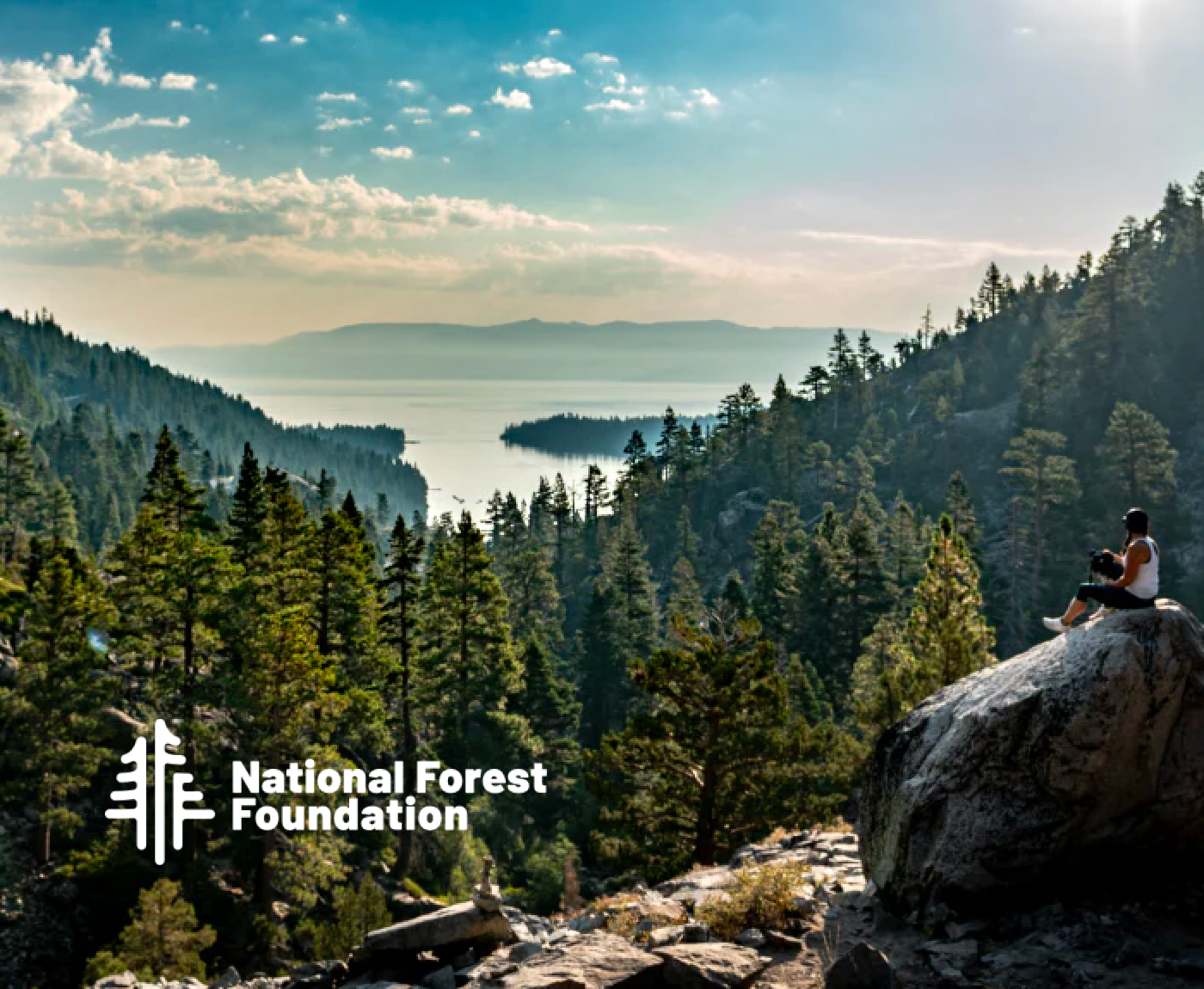 A person sitting on a rock overlooking a forest and lake, with the National Forest Foundation logo.