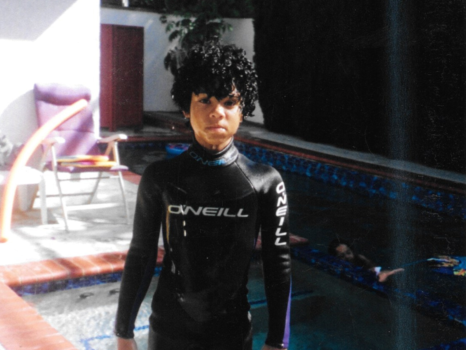 A young person in a black O'Neill wetsuit standing by a pool.