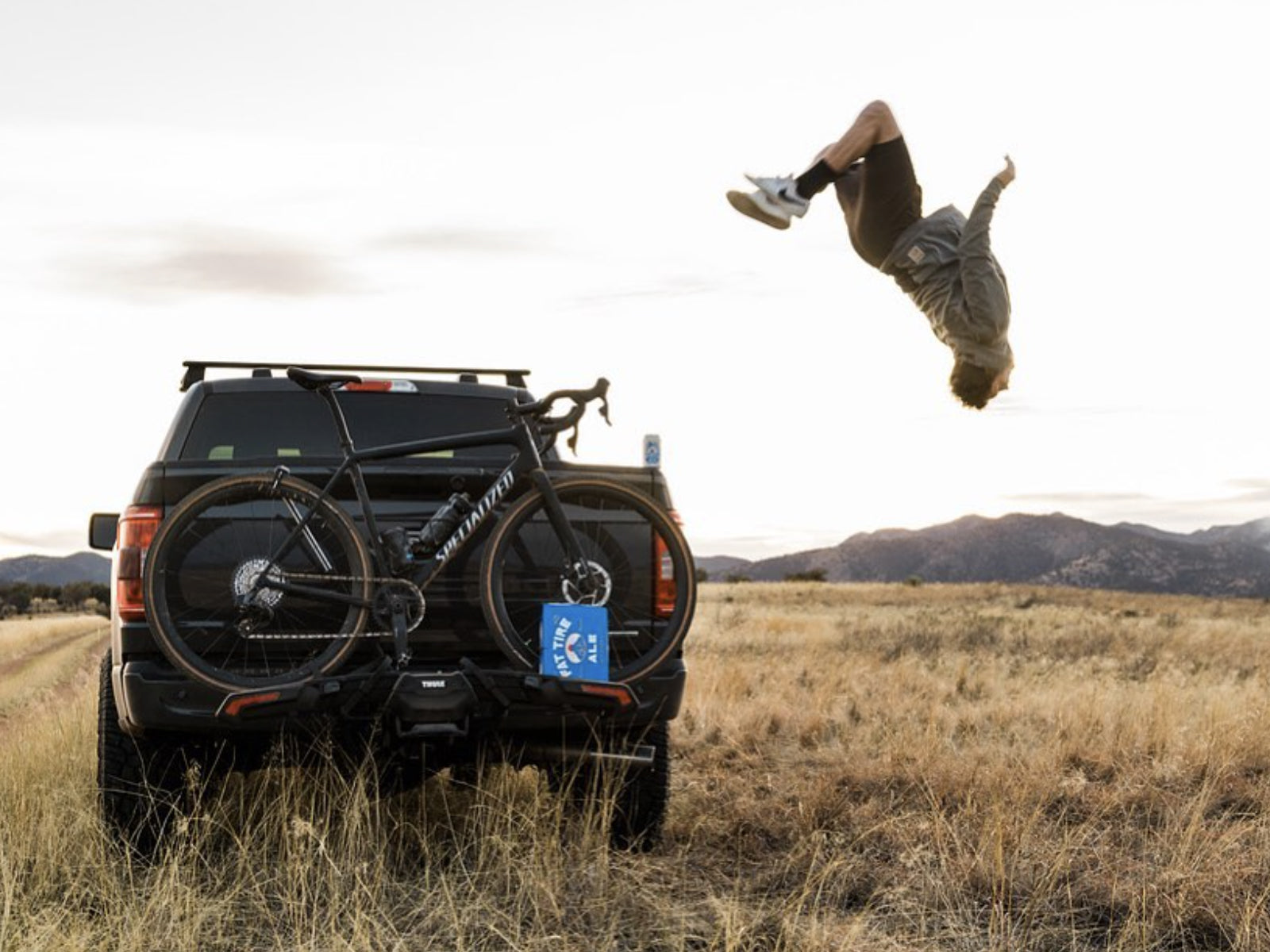 A person doing a backflip off a truck with a bicycle attached.