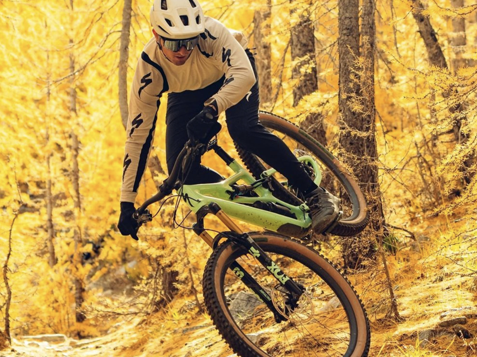 A mountain biker navigating a trail in a forest with golden autumn leaves.
