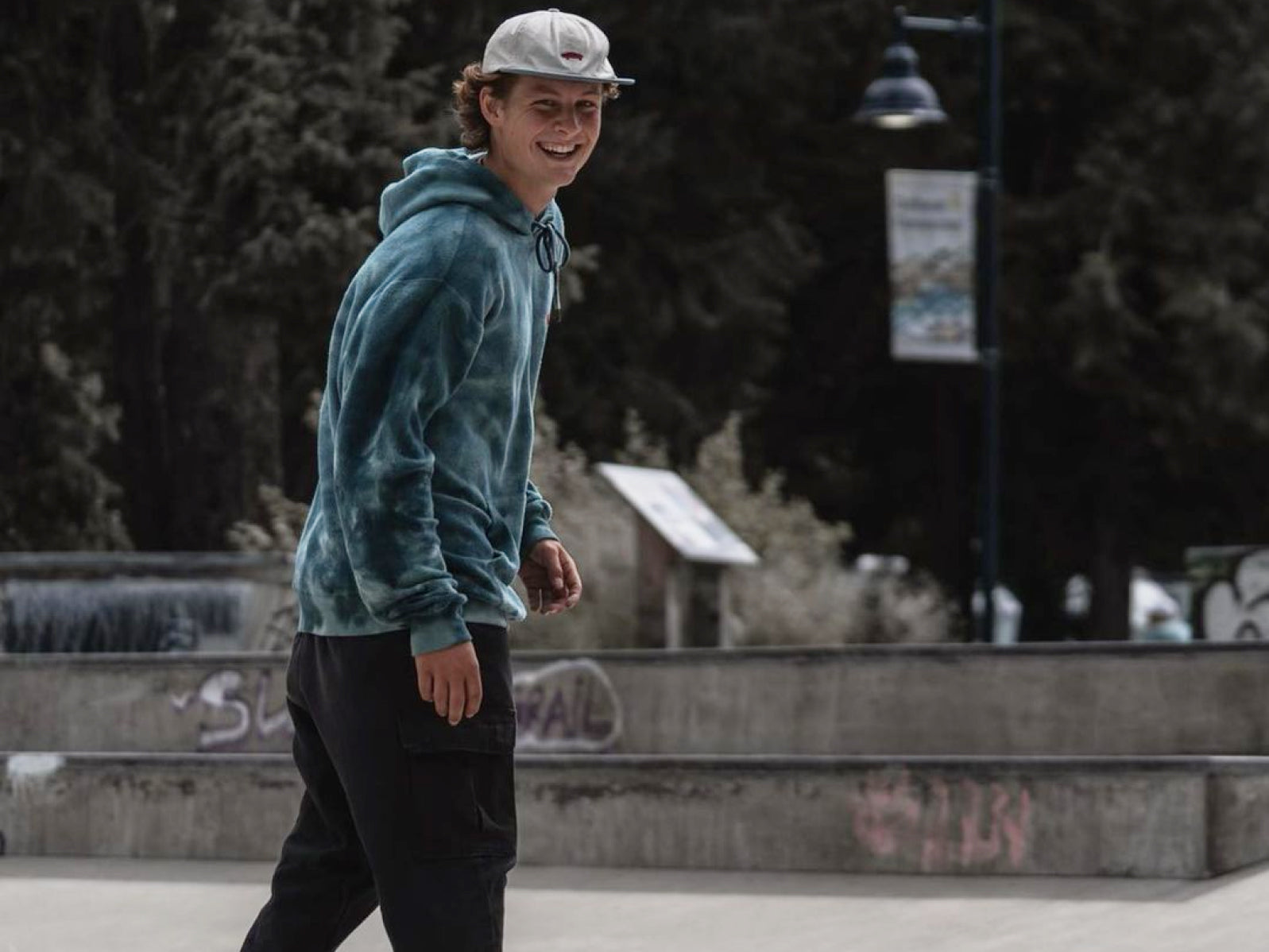 Truth Smith skateboarding in a park, wearing a blue hoodie and cap.