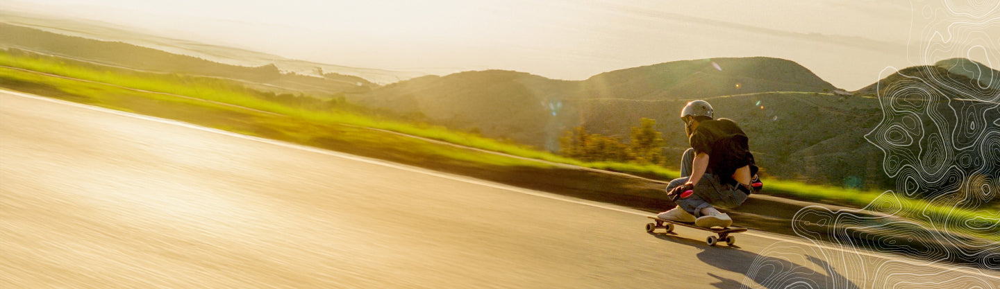 Cole Trotta skateboarding downhill on a sunny road with mountains in the background.
