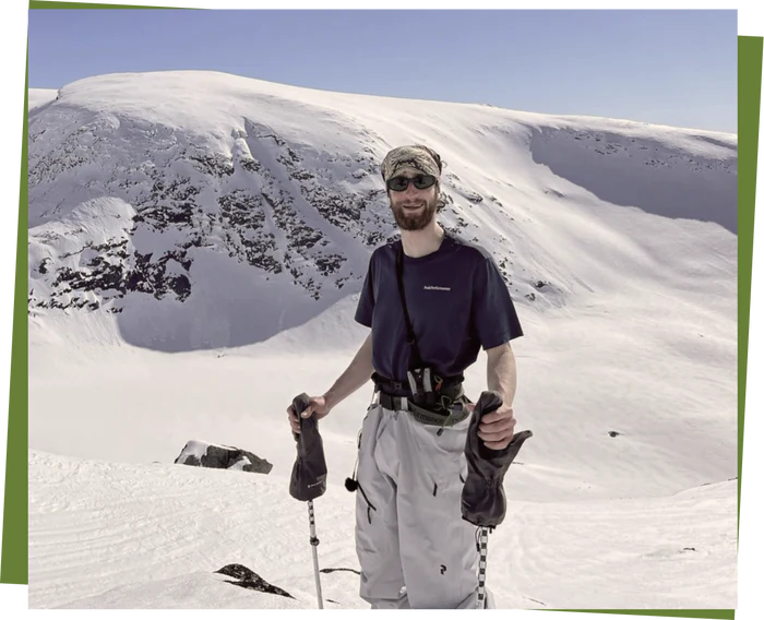 Alex Hackel skiing in the snowy Alps, smiling and holding ski poles.