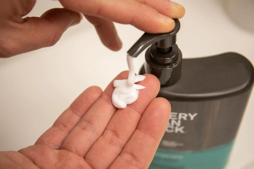 A hand dispensing grooming cream from a bottle labeled Every Man Jack.