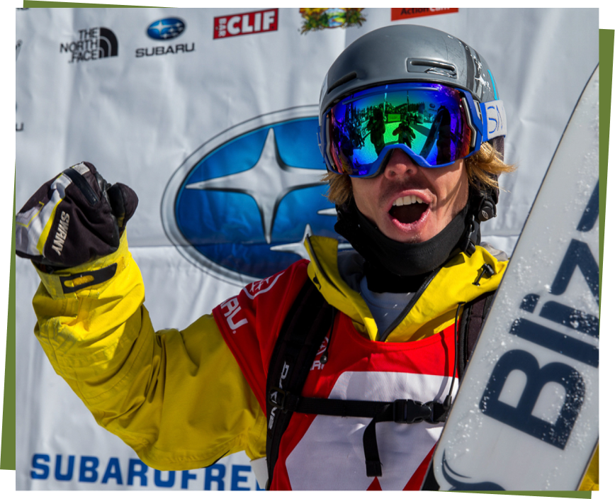 Connery Lundin celebrating after a skiing event, wearing a yellow jacket and goggles, holding a snowboard.