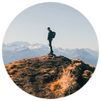 A person standing on a rocky outcrop with mountains in the background.