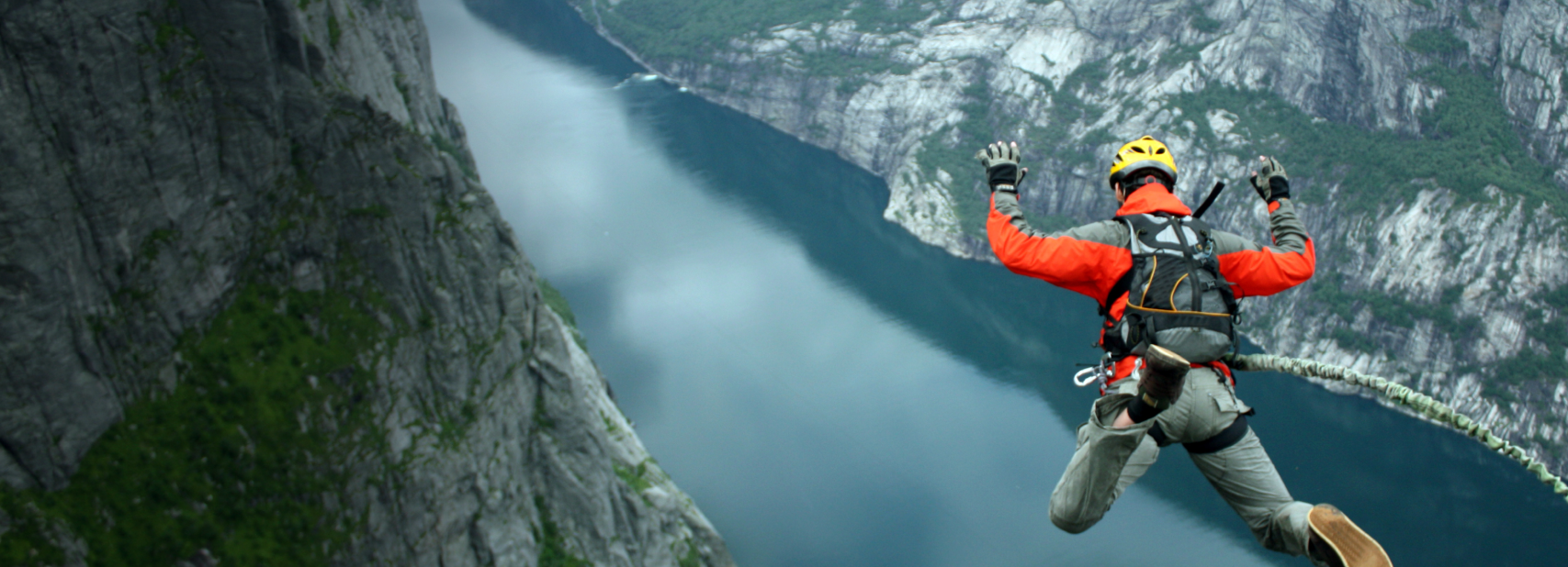 A person base jumping off a cliff into a fjord.