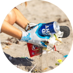 A person wearing gloves collects trash, including a can and wrappers, on a beach.