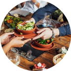 Hands exchanging bowls of salad at a dining table