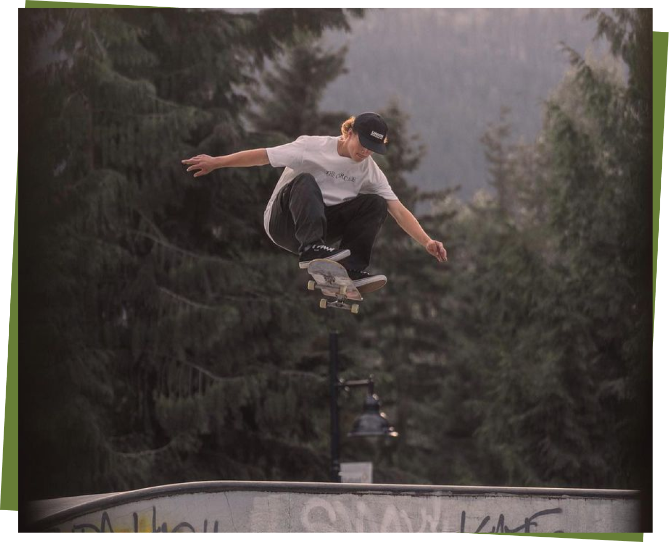 A skateboarder performing a trick in a park surrounded by trees.