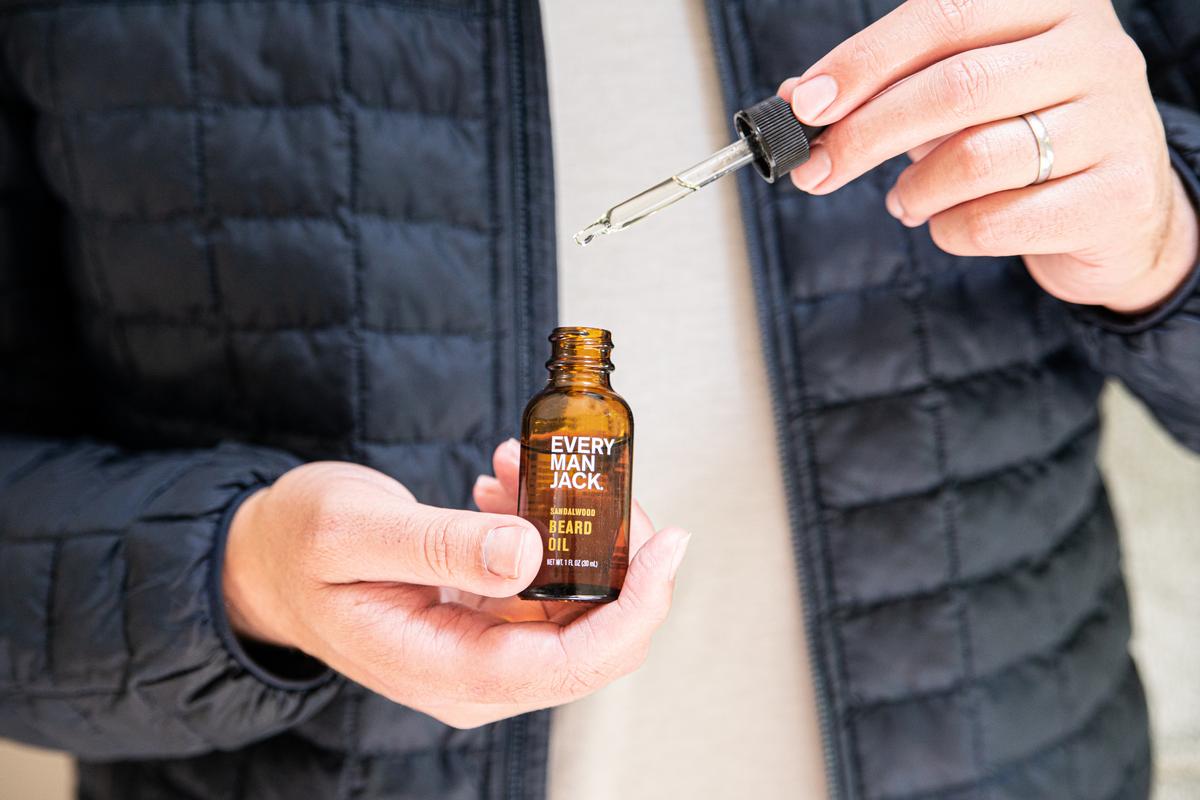 A person holding a bottle of Every Man Jack beard oil with a dropper.