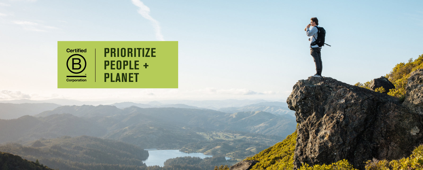 A person standing on a rock overlooking a valley with mountains, with a B Corp certification logo stating 'Prioritize People + Planet'.