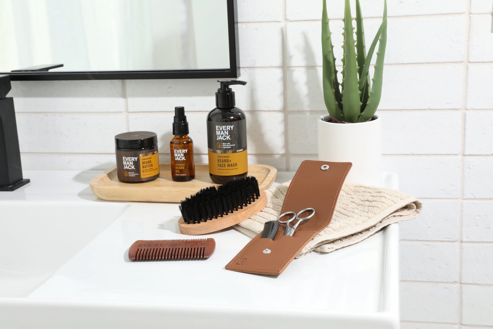 A grooming setup with Every Man Jack beard care products including a comb, scissors, and beard oil on a bathroom counter.