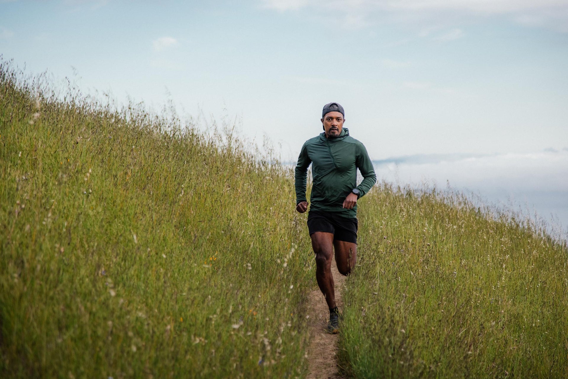 A man running on a grassy trail with hills in the background.