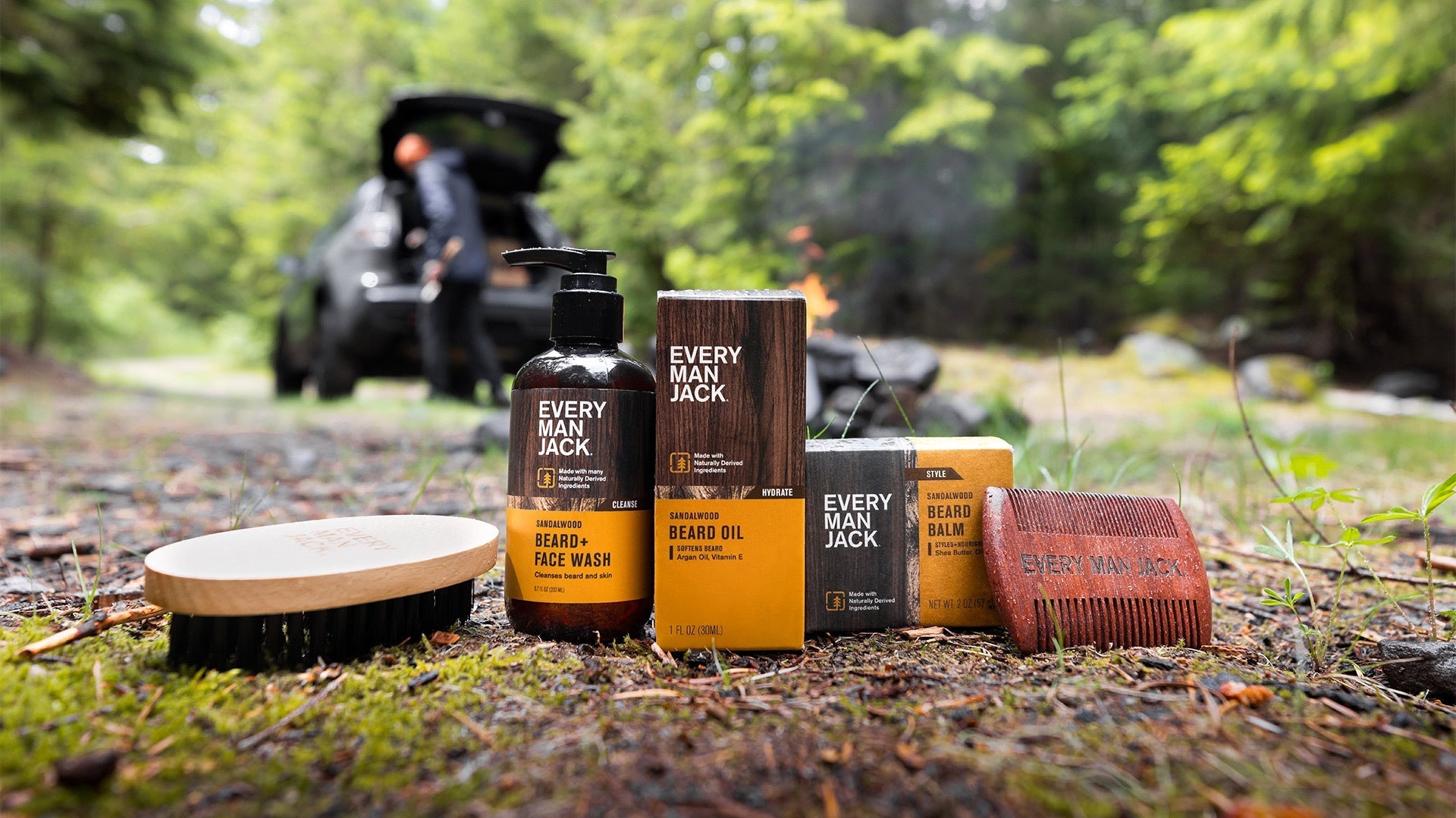 Grooming products including Every Man Jack bottles and bars arranged on forest ground