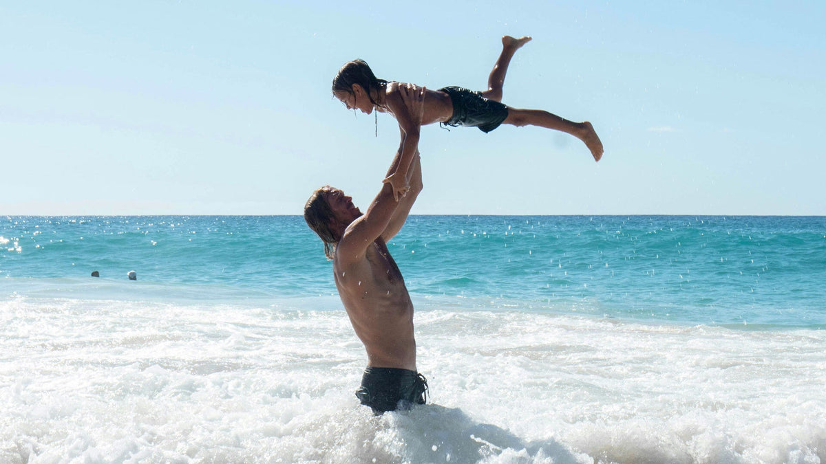 Man lifting a child above his head while standing waist-deep in ocean surf at a sunny beach