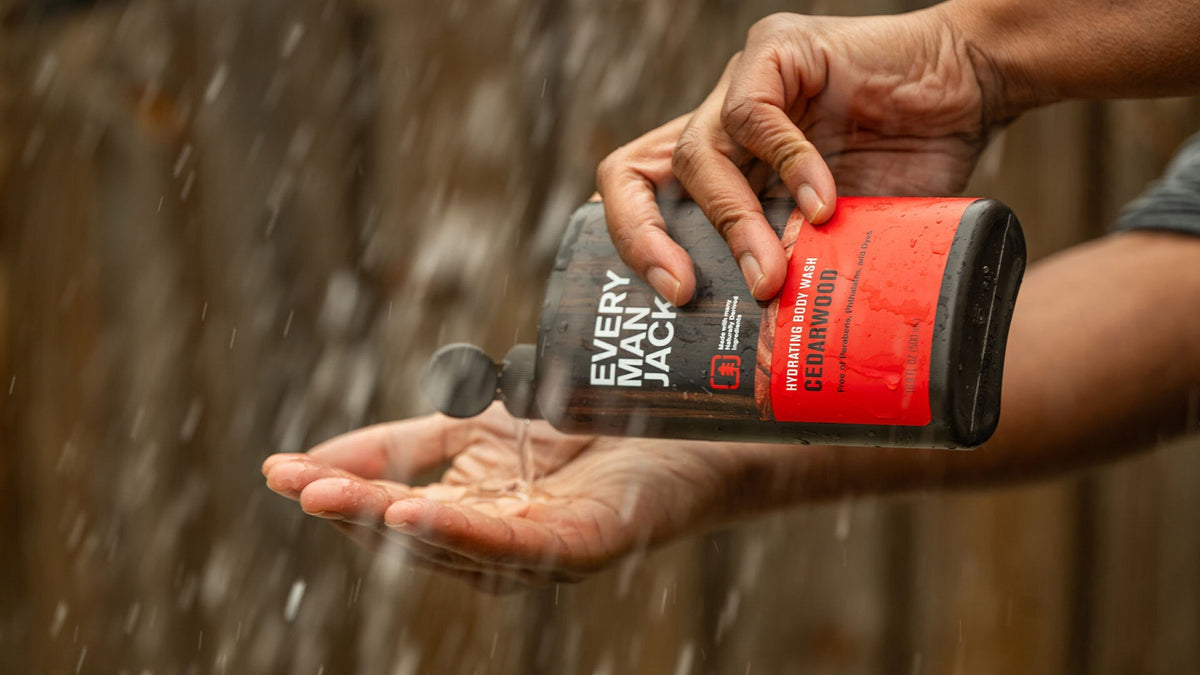 Person pouring Every Man Jack Cedarwood hydrating body wash into palm under running shower with wooden background