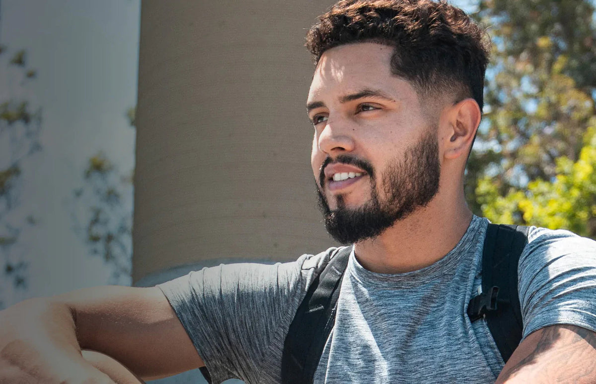 Man with a well-groomed beard wearing a gray t-shirt and backpack outdoors