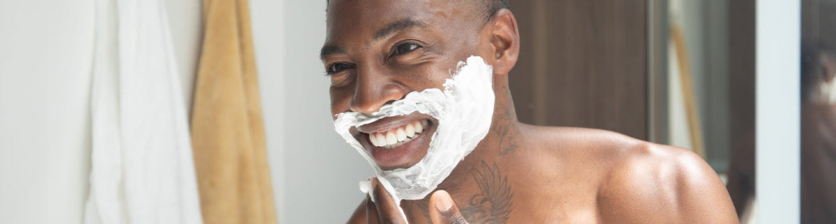 Man smiling with shaving cream on his face in a bright bathroom