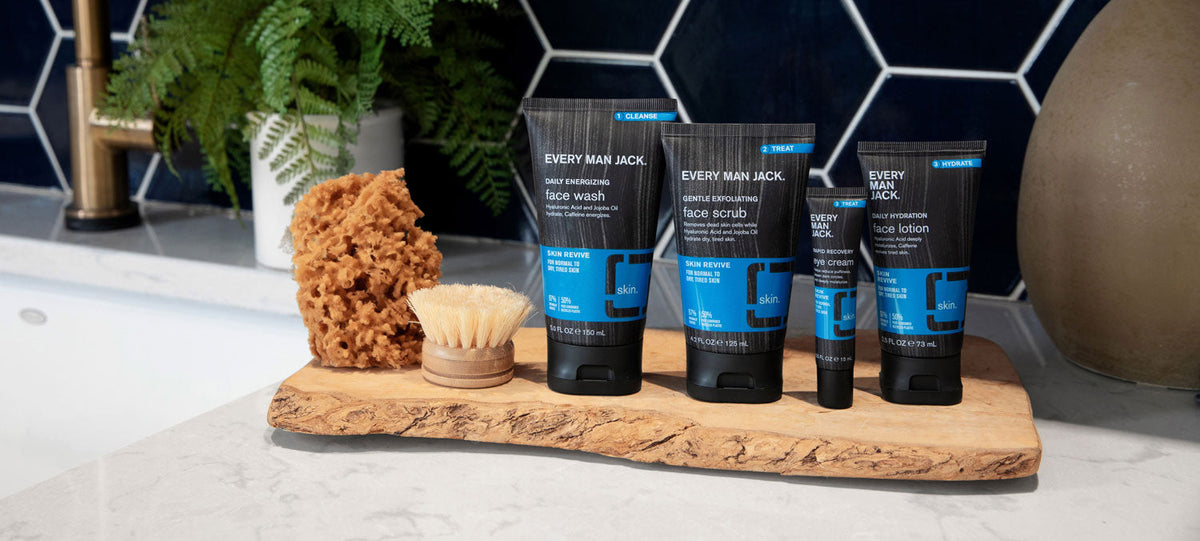 Front view of Skin Revive skincare collection showcasing four Every Man Jack tubes with blue labels and a wooden tray on a marble bathroom counter
