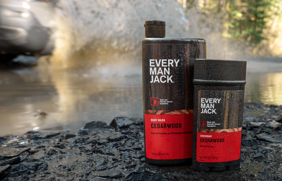 Front view of Every Man Jack Cedarwood body wash and deodorant on wet rocks with water beading and splashing background