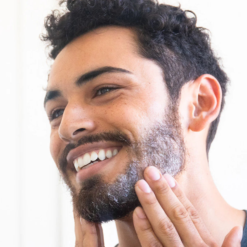 A man applying beard care product to his beard, smiling.