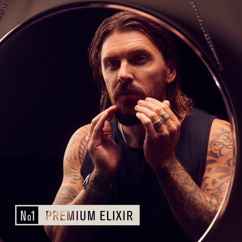 Man applying beard oil in front of a mirror with the text 'No1 PREMIUM ELIXIR' below