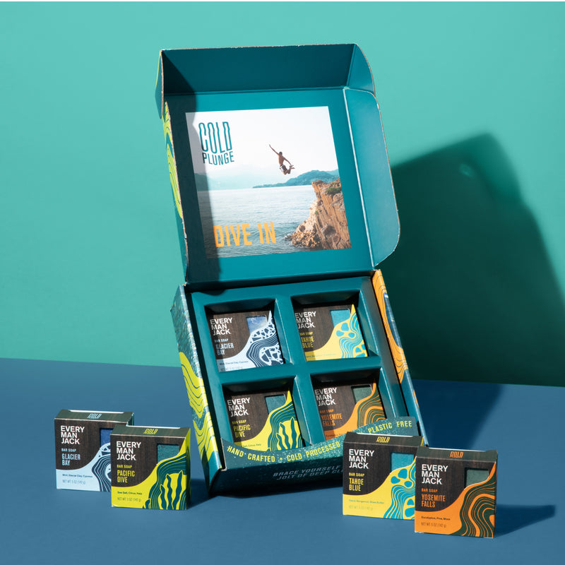 Open box of Every Man Jack Cold Plunge Kit containing 8 bars of soap labeled Glacier Bay, Pacific Dive, Tahoe Blue, and Yosemite Falls. Box interior shows a person diving with text 'COLD PLUNGE' and 'DIVE IN'.