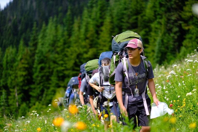 Group of young hikers ascending a hillside with backpacks in a lush green landscape
