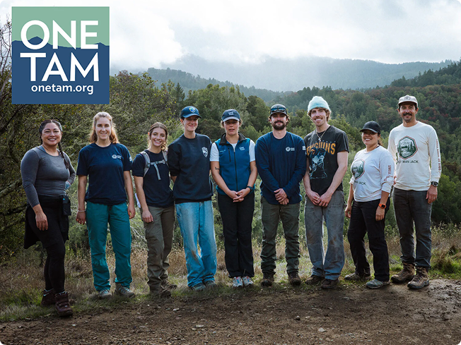 Group of One Tam volunteers standing on a trail in wooded hills with One Tam logo overlay