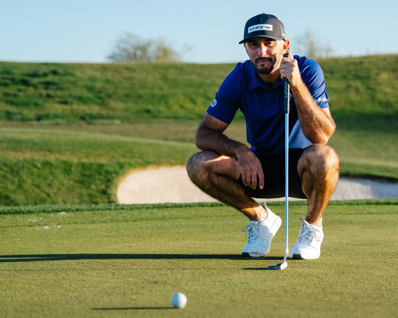Max Homa preparing to putt on a green golf course with a clear sky.