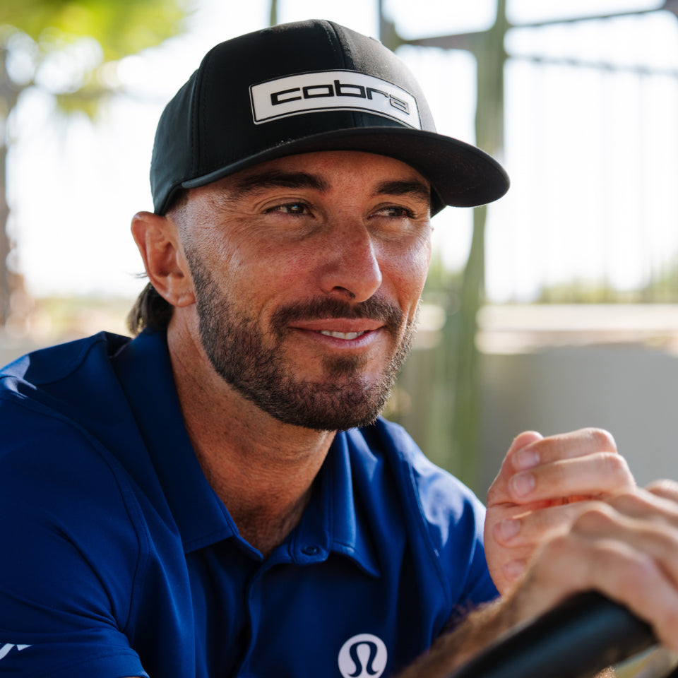 Max Homa wearing a blue shirt and black cap with 'Cobra' logo, sitting outdoors.