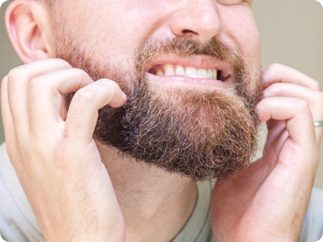 A man smiling while grooming his beard with both hands.