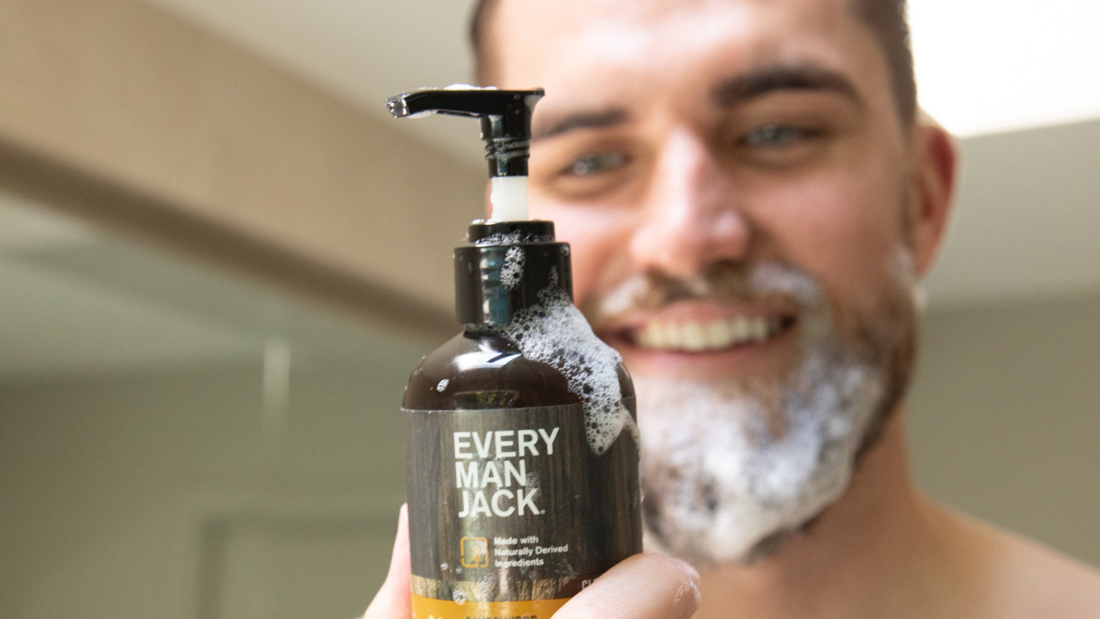 A man holding a foaming Every Man Jack grooming product in a bathroom setting.