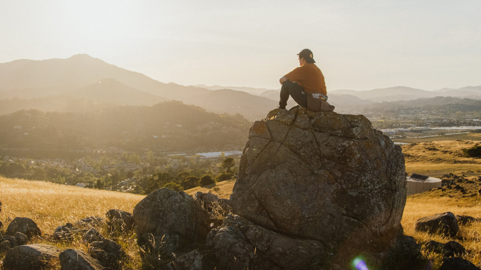 A person sitting on a rock, gazing at a sunset over mountains and valleys.