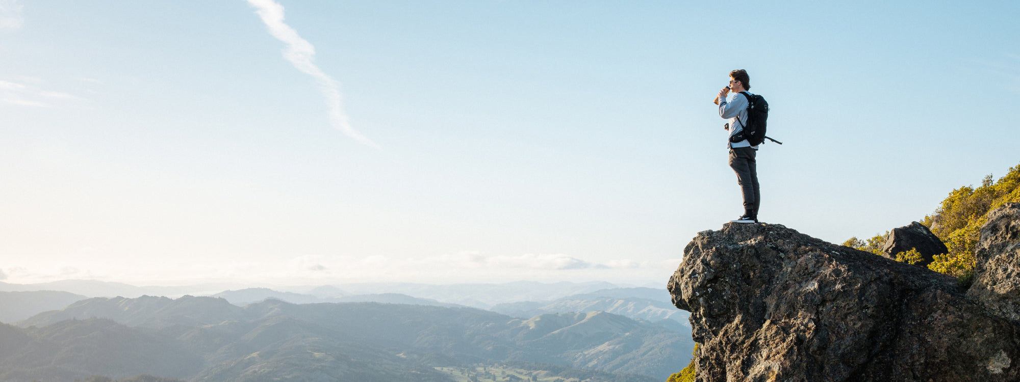 A person standing on a rock, looking out over a mountainous landscape.