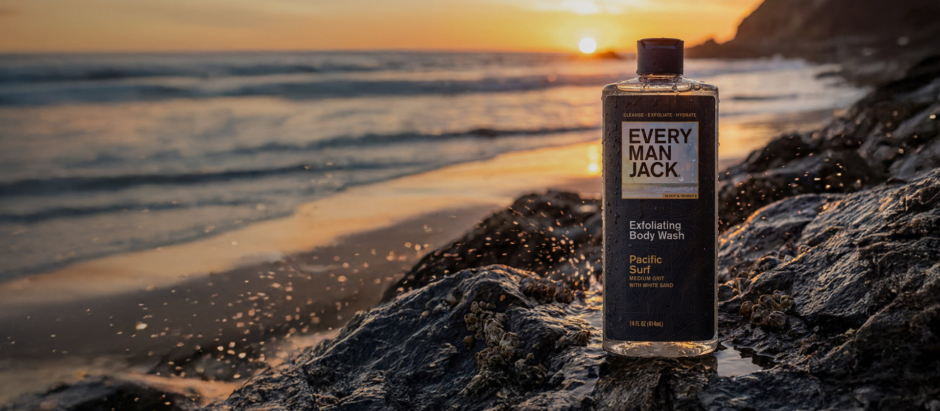 Bottle of Every Man Jack body wash on a rock by the ocean at sunset
