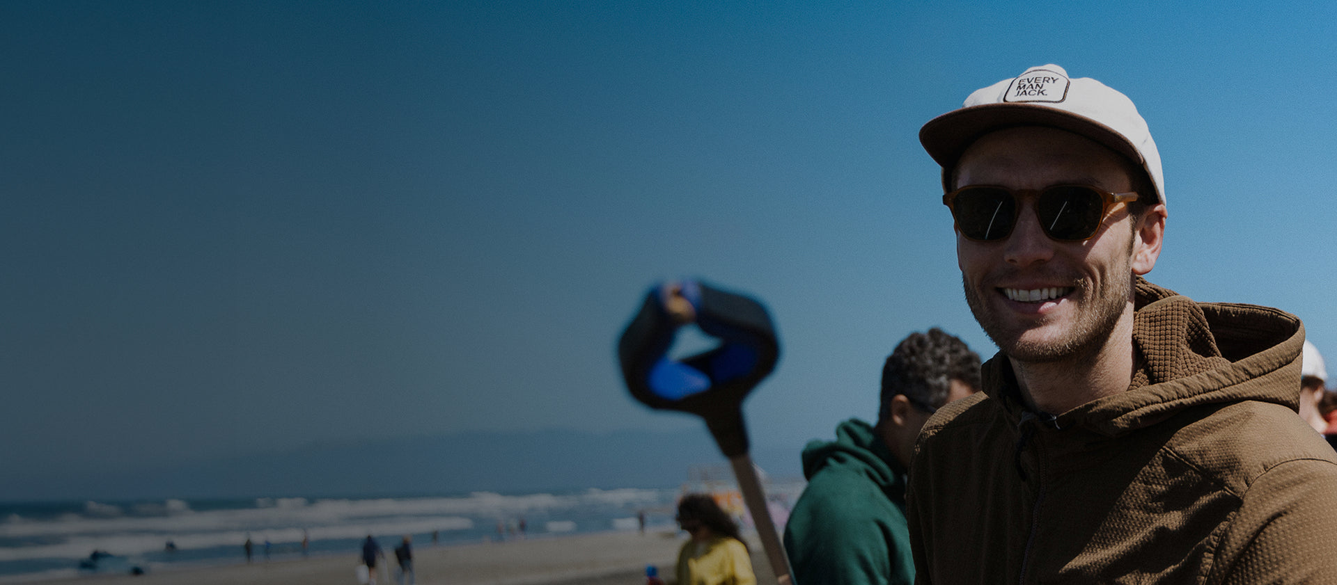 Man wearing sunglasses and a cap on a beach with a trash pickup tool