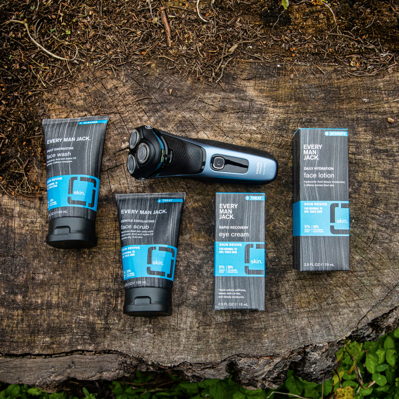 Grooming bundle with Every Man Jack face wash, face scrub, eye cream, face lotion, and a Philips electric shaver on a tree stump