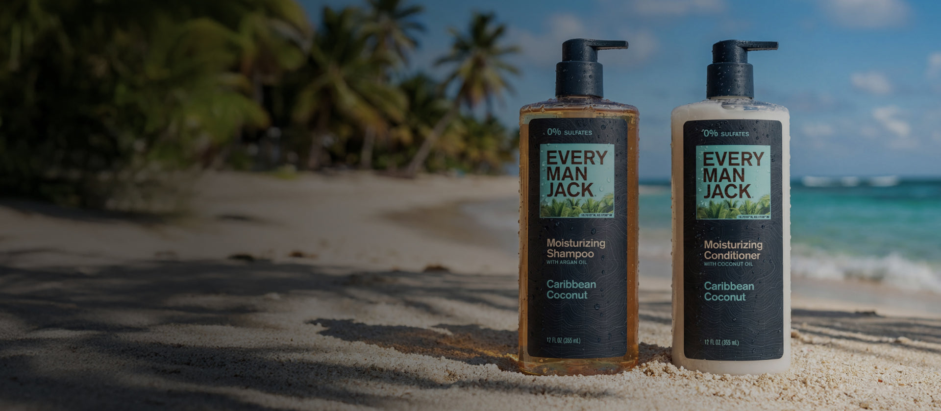 Front view of Every Man Jack Caribbean Coconut moisturizing shampoo and conditioner with pump tops and water droplets on a sandy beach background