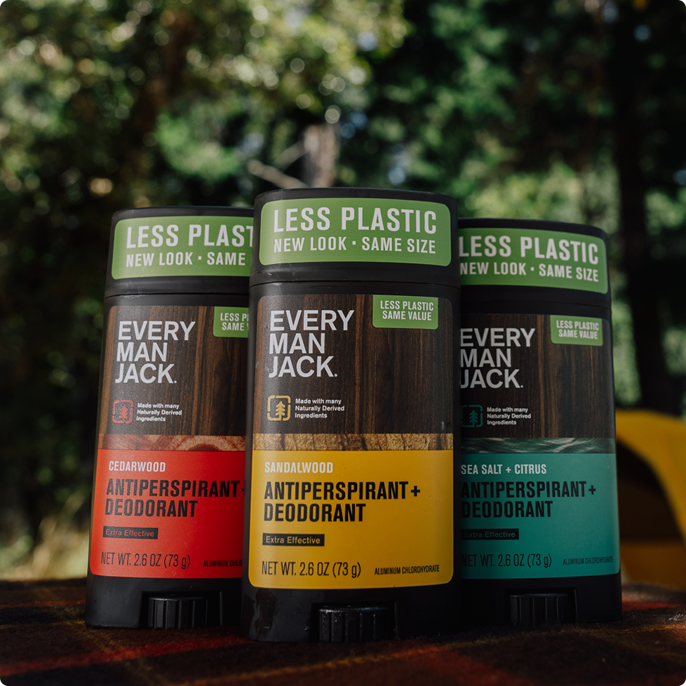 Close up of three Every Man Jack deodorant sticks highlighting Less Plastic labels and three scents against a blurred forest background
