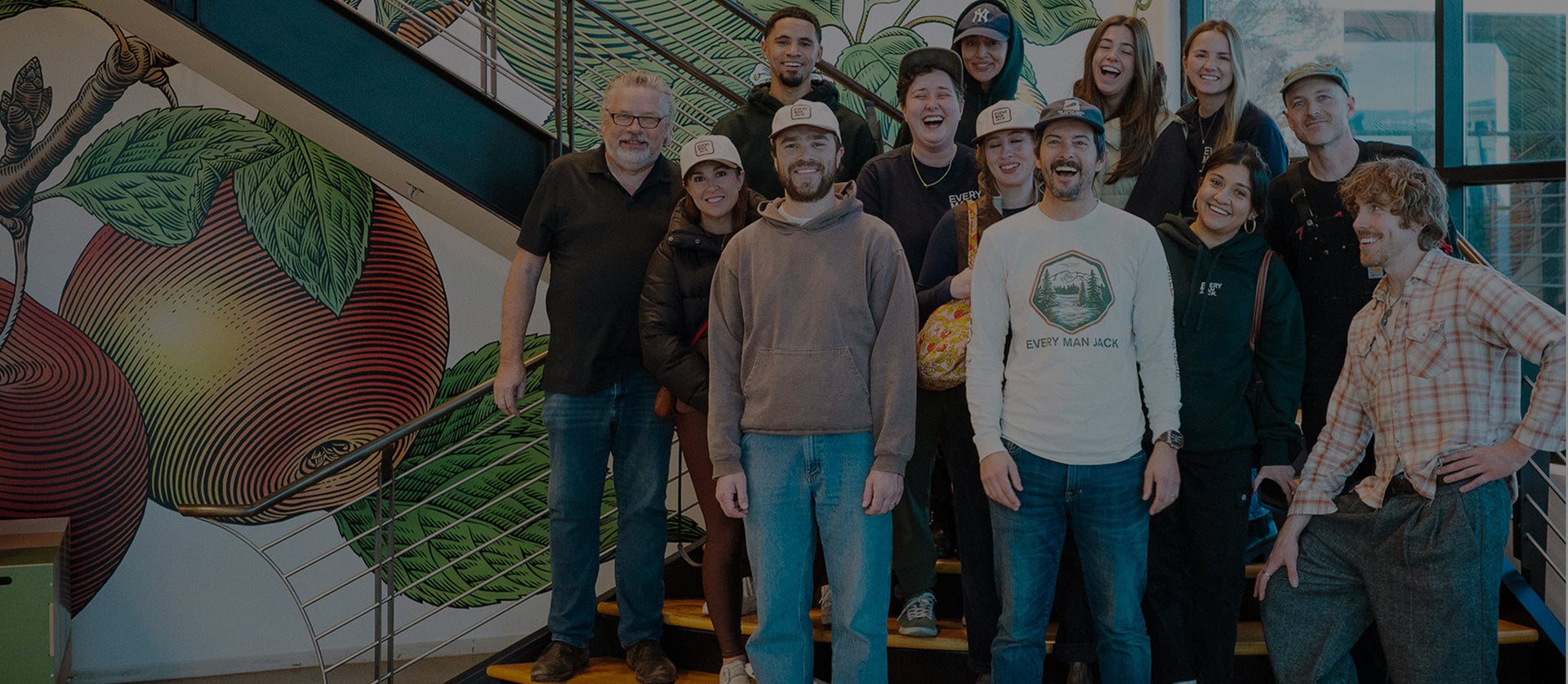 Every Man Jack team smiling on an office staircase in front of a large fruit mural