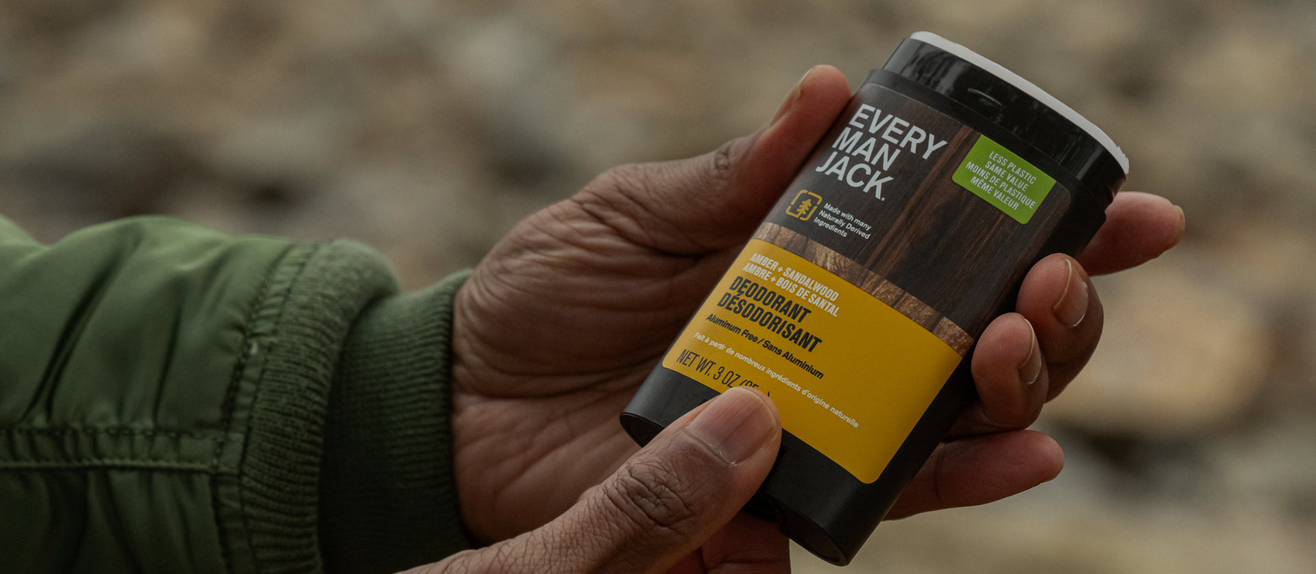 Angled view of Every Man Jack Amber + Sandalwood deodorant in hands showing yellow label and wood-grain design
