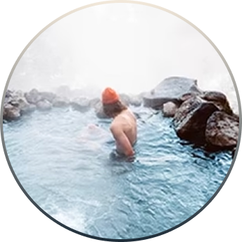 Person wearing an orange beanie soaking in a misty rocky natural pool