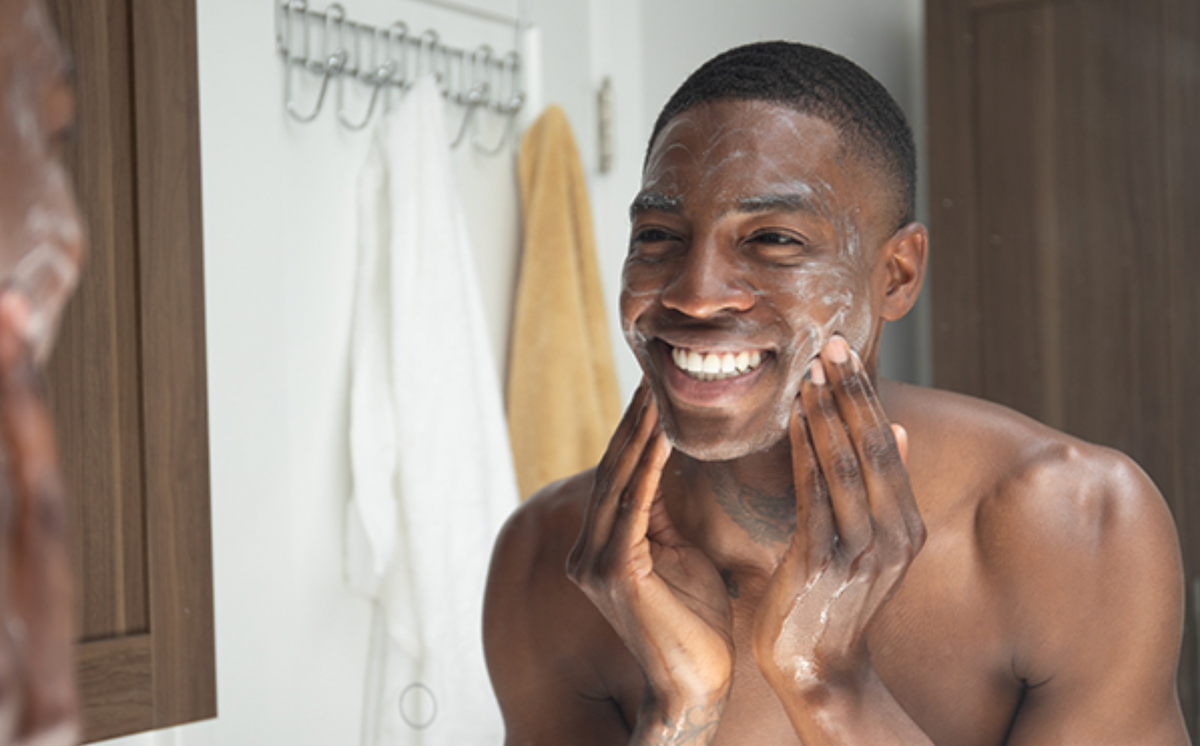 Man lathering cleanser on his face and smiling at a bathroom mirror