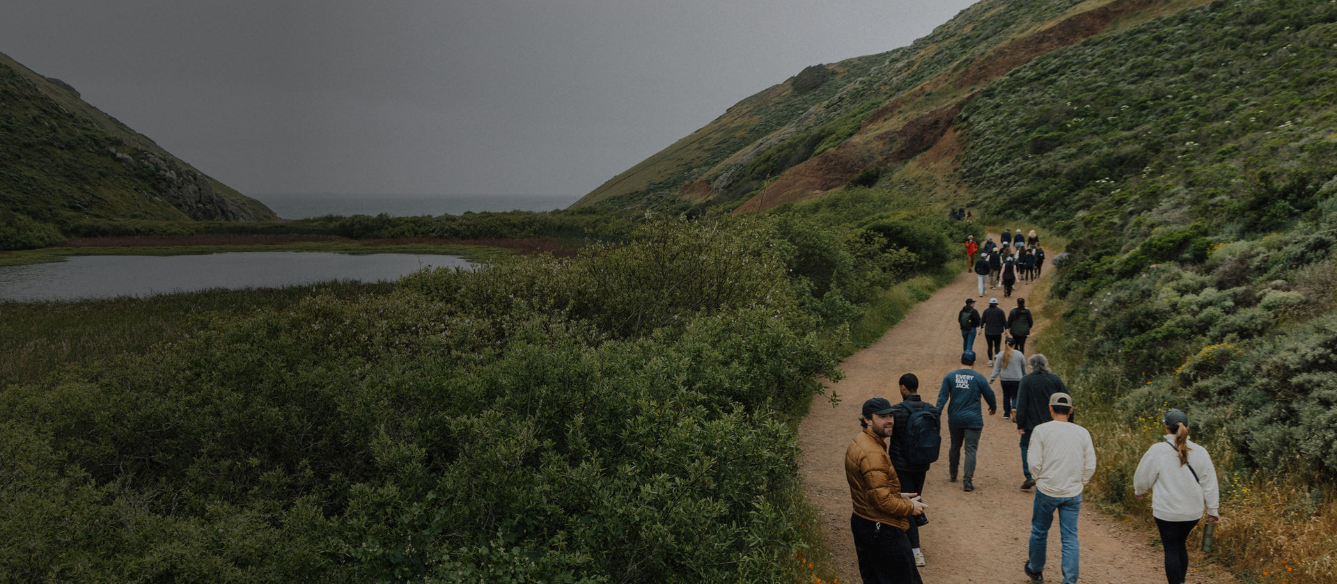 Group of people walking along a trail in a scenic, hilly area with a body of water.