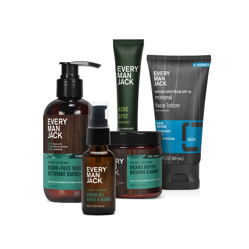 A collection of Every Man Jack grooming products including beard oil, face wash, face lotion, and beard balm in various bottles and tubes.